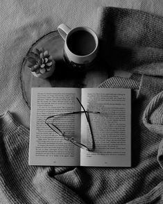 an open book with glasses on top of it next to a cup of coffee and flower