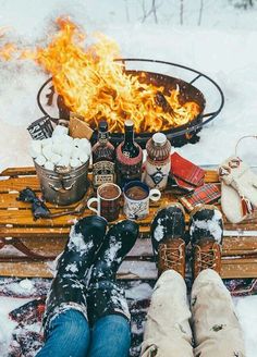 a fire pit filled with hot drinks and marshmallows next to snow covered boots