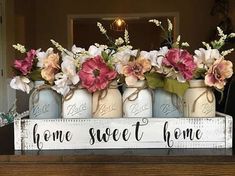 there is a sign that says home sweet home with flowers in mason jars on the mantle