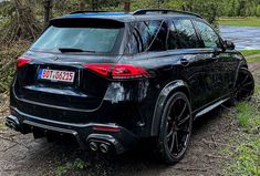 the rear end of a black suv parked on a dirt road next to a body of water