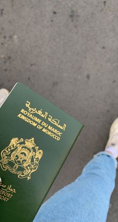 a person is holding a green passport in their left hand and wearing white sneakers on the other side