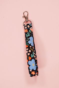 a keychain with flowers on it hanging from a metal hook in front of a pink background