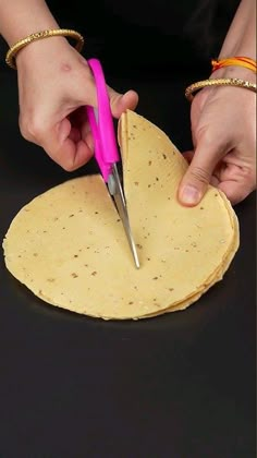 a person cutting up some tortilla with a pink scissor