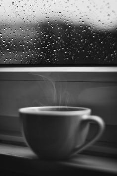 a coffee cup sitting on top of a window sill next to a rain covered window