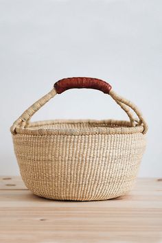 a woven basket with a wooden handle sitting on top of a wood table in front of a white wall