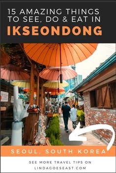 an outdoor market with orange umbrellas and people walking down the street in front of it