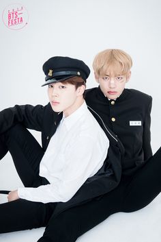 two young men sitting next to each other in black and white outfits, one wearing a sailor's hat