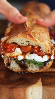 a person is holding a sandwich with tomatoes and cheese on it while standing on a cutting board