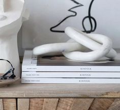 a stack of books sitting on top of a wooden table next to a white sculpture