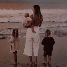 a woman and two children are standing on the beach watching the waves in the ocean