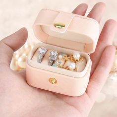 a hand holding an open ring box with several rings in it and pearls around the edges