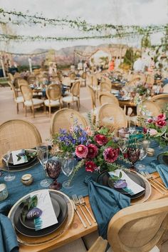 a table set up with place settings and flowers in vases on the tables at an outdoor event