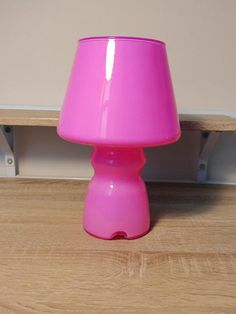 a pink lamp sitting on top of a wooden floor next to a white wall and shelf