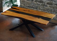 a wooden table sitting on top of a floor next to a stone wall and potted plant