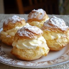 four pastries on a plate with powdered sugar and icing sitting on a table