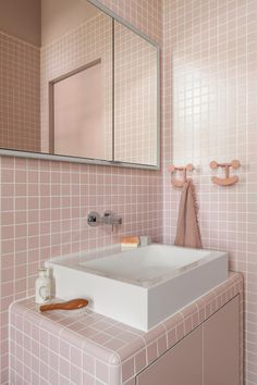 a bathroom with pink tiled walls and flooring, including a white square sink under a large mirror