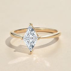 a gold ring with a princess cut diamond on it's side, sitting on a beige surface