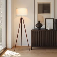 a floor lamp sitting on top of a wooden stand next to a window and framed pictures