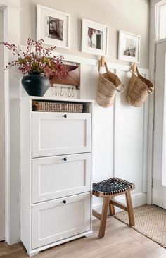 a white cabinet with baskets and pictures on the wall next to a stool in front of it