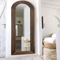 a large mirror sitting on top of a white wall next to a basket filled with towels