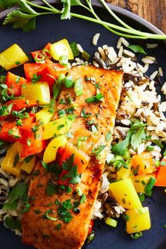 a blue plate topped with fish and rice next to veggies on a wooden table