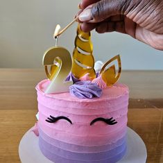 someone is lighting candles on a cake decorated with pink and purple icing, unicorn face