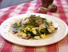 a white plate topped with salad on top of a red and white checkered table cloth