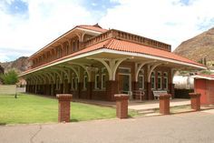 an old train station in the desert with mountains in the backgrouds and grass on either side