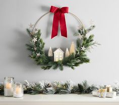 a christmas wreath hanging on the wall above a mantle with candles and ornaments around it