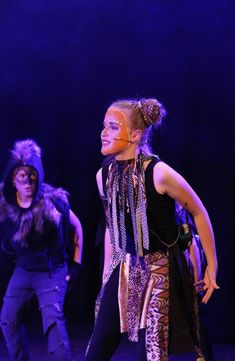 two young women in costume on stage with one woman standing behind her and the other is wearing