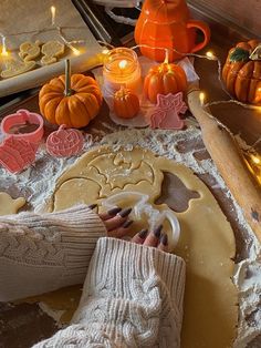 a person is decorating pumpkins and cookies on a table with candles in the background