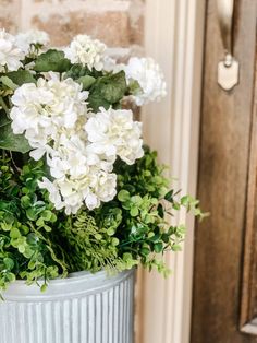 a white bucket filled with flowers next to a door