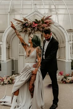 a man and woman standing next to each other in front of a building with lots of flowers