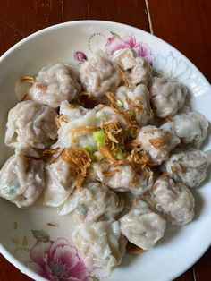 a white bowl filled with dumplings covered in sauce and toppings on top of a wooden table