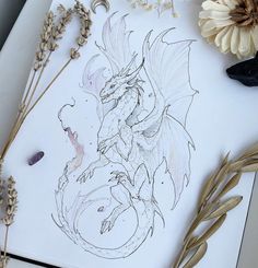 a drawing of a dragon sitting on top of a table next to some dried flowers