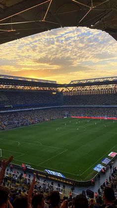 a soccer stadium filled with lots of people watching the sun go down on an empty field