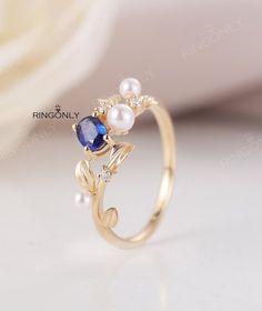 a gold ring with blue and white stones on it, sitting next to a flower