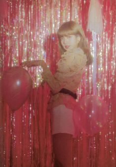 a woman standing in front of a red curtain with balloons