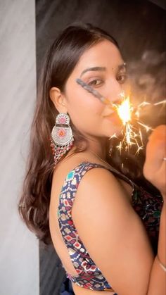 a woman holding a sparkler in her right hand and wearing earrings on top of her head