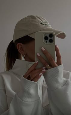 a woman taking a selfie with her cell phone in front of her face and wearing a baseball cap