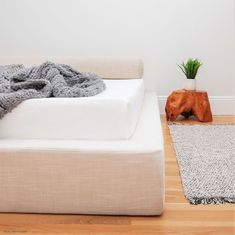 a white bed sitting on top of a hard wood floor next to a potted plant