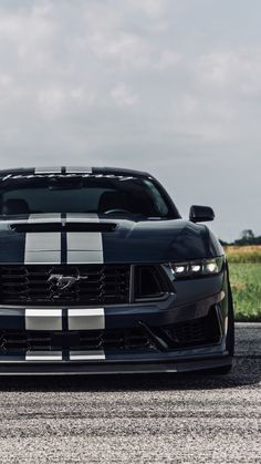 the front end of a black sports car on a road with grass in the background