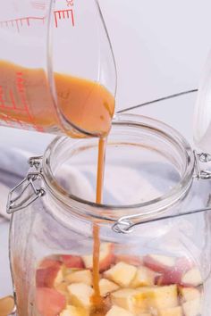 someone pouring orange juice into a jar filled with sliced apples and other fruit in it