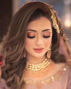 a woman with long hair wearing a pink dress and gold jewelry is looking down at her face