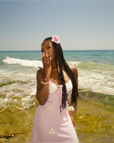 a woman standing on top of a beach next to the ocean holding her hands up