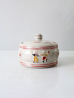 a white ceramic covered dish with horses on it's side and red trim around the edge