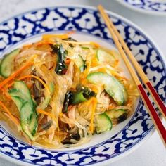 a blue and white plate topped with noodles and veggies next to chopsticks