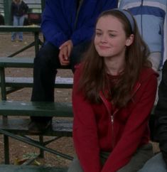 a woman sitting on top of a green bench next to another person in a blue jacket