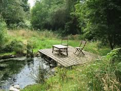 two wooden chairs sitting on top of a wooden bridge over a small creek in the woods