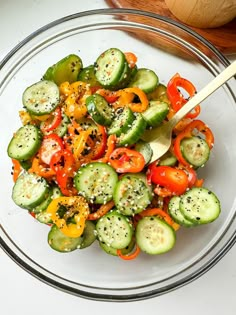 a glass bowl filled with cucumbers and peppers on top of a table next to a wooden spoon